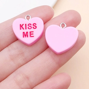 Nahaufnahme von rosa Herzanhängern aus Harz mit KISS ME Schriftzug in der Hand gehalten