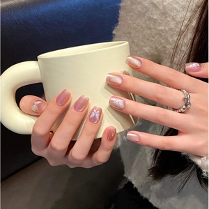Rosa-lila Aurora Katzenaugen-Nägel mit Schmetterlings-Design am weißen Becher gehalten