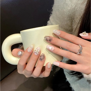 Pink press-on nails with bow and heart accents on hands holding a yellow mug
