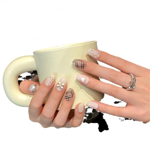 Elegant handmade short press-on nails with bow, heart, and pearl accents on light beige base