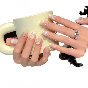 Rosa Ombré-Kunstnägel mit Perlenherzen und Schleifen an einer Hand mit Tasse
