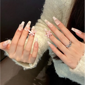 Faux ongles mats roses avec nœuds et breloques flacons de parfum sur mains de mannequin