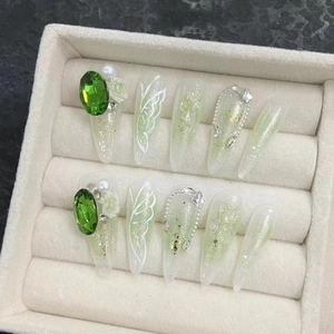 Handmade press-on nails with green butterfly designs, pearls, and emerald crystals