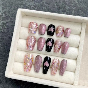 Pink cat-eye press-on nails with glitter and heart accents in a beige display box