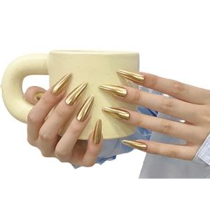 Glossy golden metallic mirror finish stiletto press-on nails shown on hands holding a cup