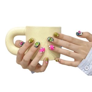 Handmade press-on nails with olive green and pink stones shown on a mug handle