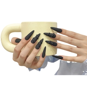 Matte black long pointed press-on nails with 3D gothic snake design on a ceramic cup