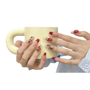 Handmade strawberry press-on nails with red French tips and pearl accents on a yellow mug