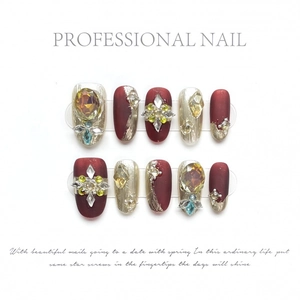 Luxury handmade press-on nails in matte dark red and gold with amber rhinestones