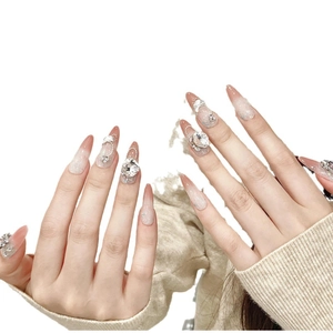 Long almond press-on nails with nude pink gradient, glitter, and heart rhinestones