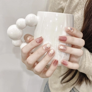Detail of short square press-on nails with pink floral daisy patterns on white ceramic cup