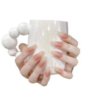 Long coffin press-on nails with peach ombre blush design held on a white pearl mug