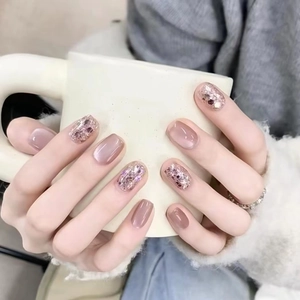 Short square pink press-on nails and silver glitter accents on hand holding a mug