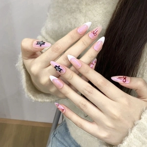 Pink almond French press-on nails with black doodle patterns and red ribbon bow accents