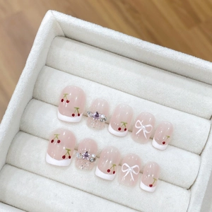 Handmade press-on nails set with red cherry patterns and white bows on velvet tray