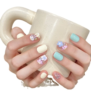 Faux ongles courts ovales vert menthe et jaunes avec fleurs 3D posés sur un mug décoré