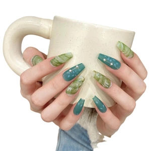 Handmade emerald green marble press-on nails with floral art and pearls on a ceramic cup