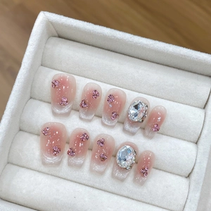 Handmade pink ombre press-on nails with floral rhinestones and glitter in a display box