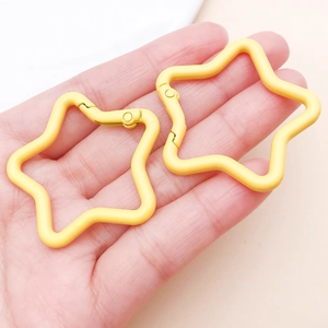 Detail of hand holding two bright yellow star-shaped metal keychains with spring gate hooks