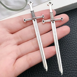 Detail of hand holding vintage silver sword charms with antique finish for DIY jewelry