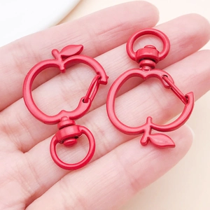 Macro detail of two red apple-shaped metal lobster clasps with rotating rings