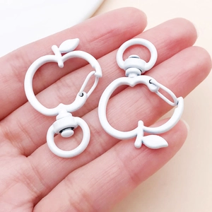 Close-up of white apple-shaped swivel lobster clasps held in hand for DIY crafts