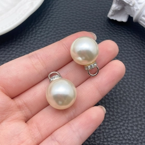 Dettaglio di ciondoli con perle ABS bianco crema e passanti in metallo argentato con strass