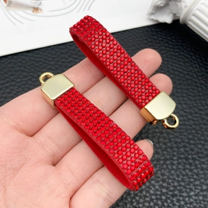 Detail van rode strass-hangers met gouden metalen sluiting op zwart leer
