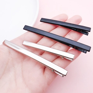 Hand holding silver and matte black metal duckbill clips for DIY hair accessories