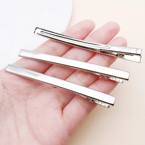 Macro view of silver duckbill hair clips held by hand showing KOREA engraving detail
