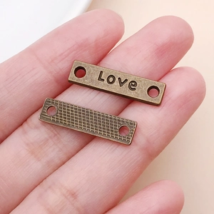 Detail eines antiken Bronze-Verbinders mit Love-Gravur und Gittertextur für DIY-Schmuck