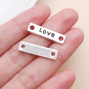 Detail von silbernen 'Love' Anhängern mit Doppelbohrung und strukturierter Rückseite