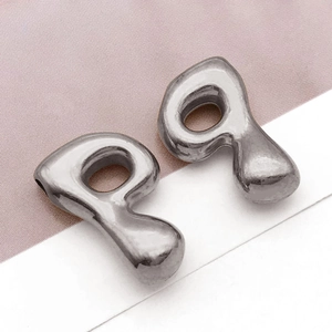 Makroaufnahme von silbernen Liquid-Metal-Ohrringen mit poliertem Finish auf sanftem Grund