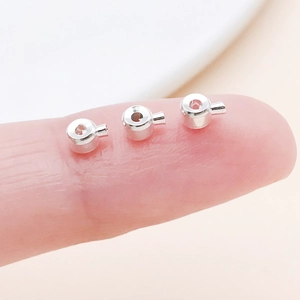 Macro view of tiny silver jewelry crimp beads on a fingertip for size comparison
