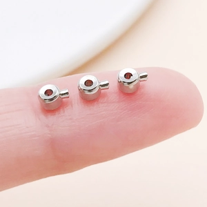 Macro view of small copper crimp beads for jewelry making held on a fingertip for scale