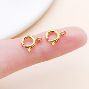 Macro view of two 6mm gold spring ring clasps for jewelry making on a fingertip