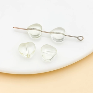 Macro detail of 10mm light green heart glass beads on a white plate for DIY jewelry