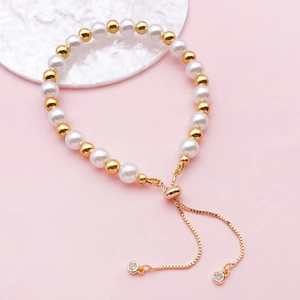 Adjustable pearl and gold bead bracelet with cubic zirconia charms on pink backdrop