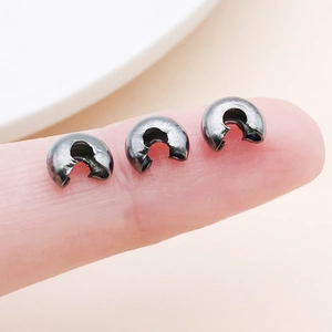 Macro shot of gun-black C-shape fold-over jewelry crimp beads held on fingertip