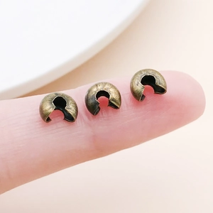 Macro view of small brass crescent crimp covers held on fingertip for DIY jewelry making