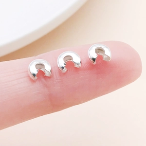 Macro shot of silver C-shaped crimp covers on finger for jewelry making size reference