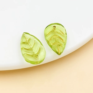 Close-up of translucent green glass leaf charms with gold leaf veins for DIY jewelry