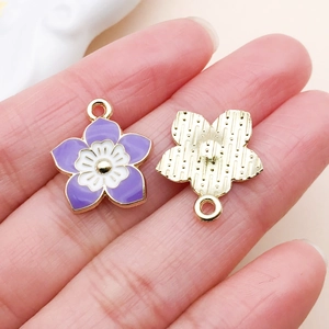 Detail view of purple enamel flower charms for DIY jewelry making with gold back texture