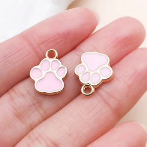 Close-up of pink cat paw charms with gold metal edges shown on fingertips for size scale