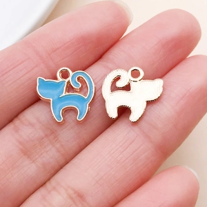 Macro shot of blue enamel cat charms showing front and back textures on fingertips