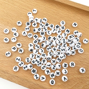 Close-up of white 6mm acrylic alphabet beads with black letters on a wooden tray