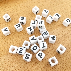 Close-up of white 6mm square acrylic letter beads with black initials on wood surface