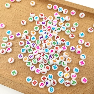 Close-up of white acrylic alphabet beads with colorful letters on a wooden tray for DIY crafts
