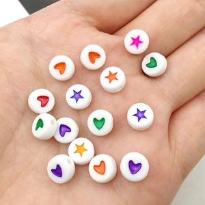 Close-up of white acrylic beads with colorful heart and star patterns held in a hand