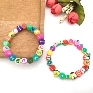Détail de bracelets colorés en argile avec perles alphabet et charms fruits